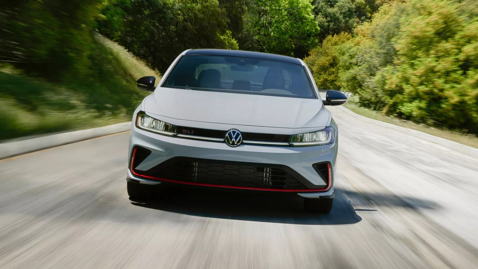 2026 Volkswagen Jetta GLI front grille driving shot featuring red horizontal accent stripe and GLI badge